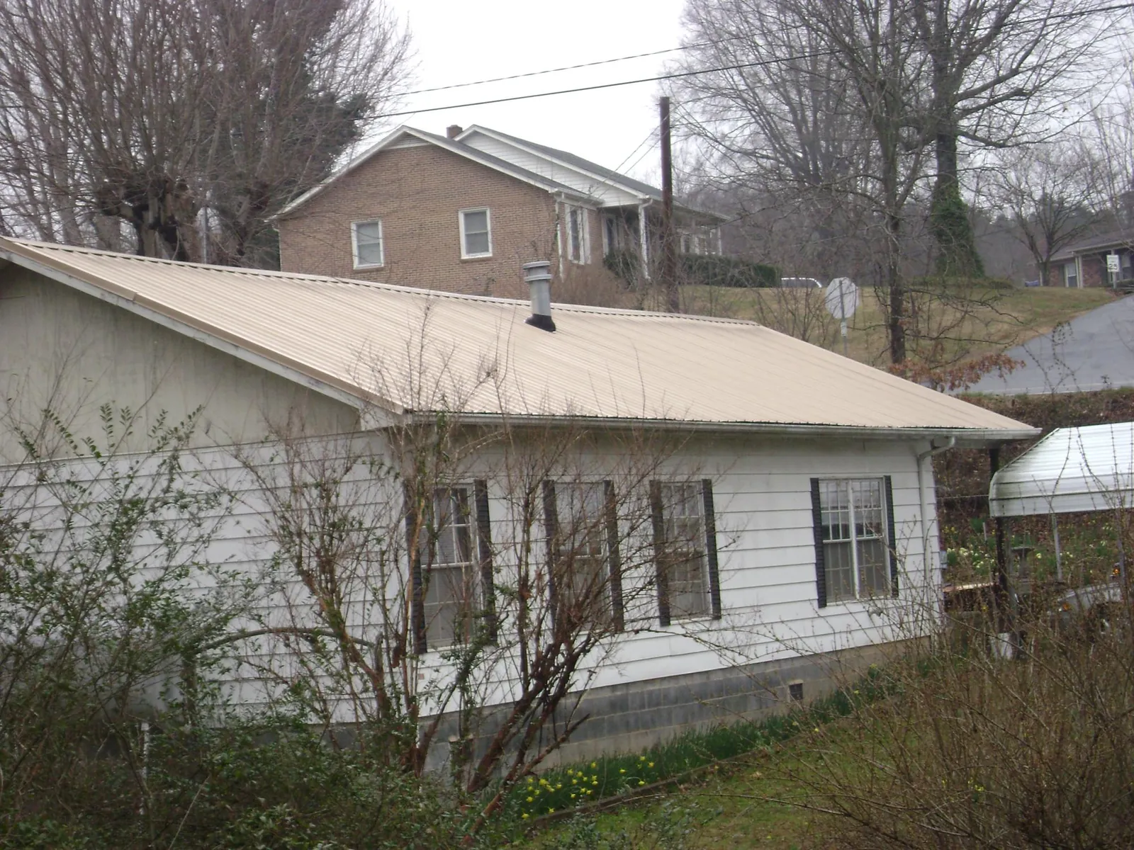 Tan metal roof on a white sided house set into a hillside — Commercial Roofing by Roofing Brothers in Batesville
